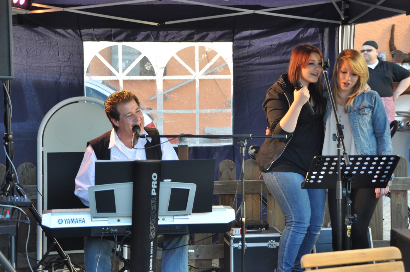 Zwei Sängerinnen mit Musiker Adrian Marko Zwei Sängerinnen stehen am Mikrofon, während ein Pianist spielt. Bühnenatmosphäre.
