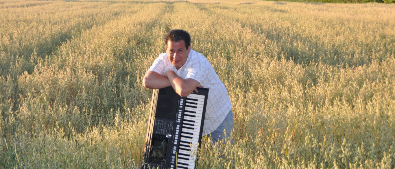 Adrian Marko Ati Ihr Musiker mit Keyboard Eine Person lehnt an einem Keyboard in einem goldenen Getreidefeld.